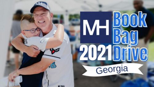 Two people hug at the 2021 MH Book Bag Drive in Georgia, an outdoor event with tents and attendees.