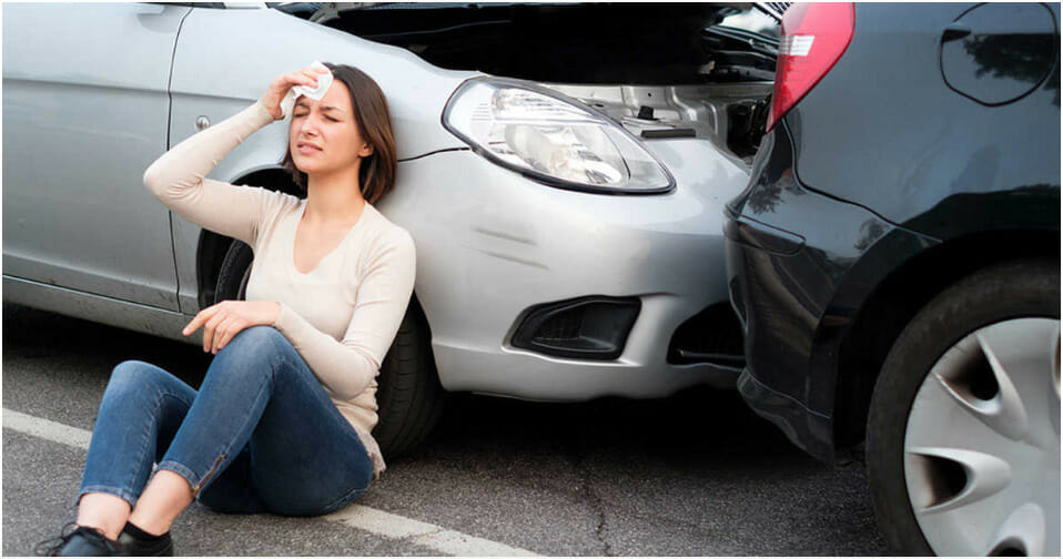 A woman sitting on the ground next to her car after a personal injury auto accident.