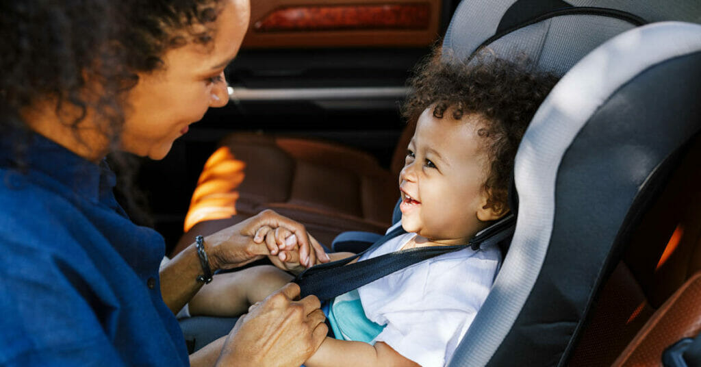 A woman is securing a child in a car seat.
