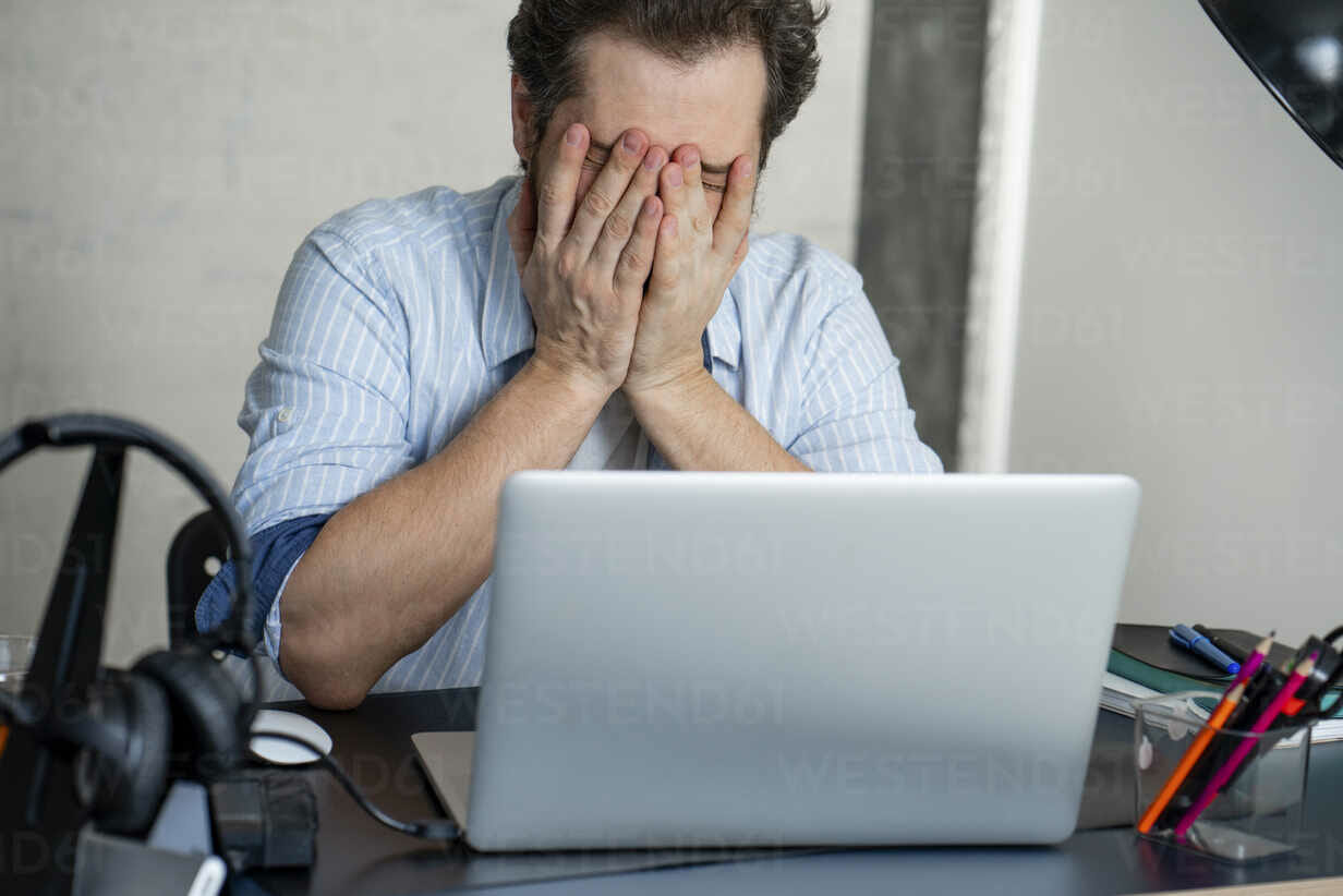 The Mike Hostilo Law Firm - A man covering his face with his hands while working on his laptop after experiencing a personal injury from an auto accident.