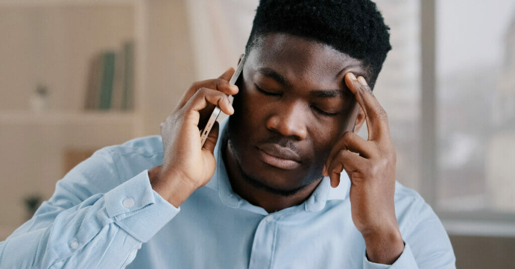 A black man discussing a personal injury case over the phone with his hand on his head.