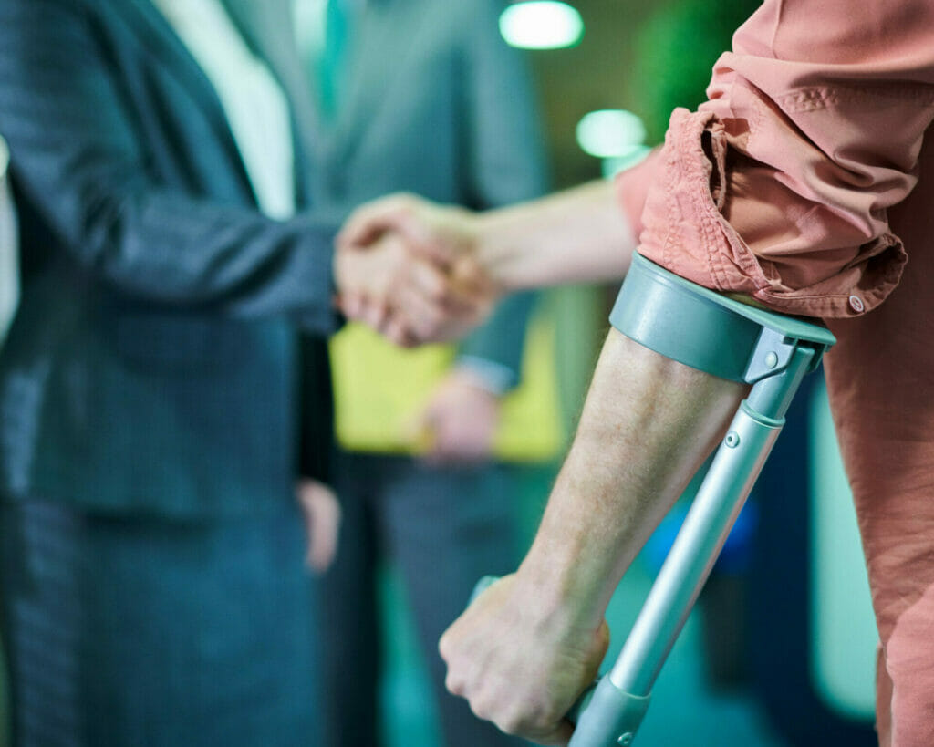 A lawyer shakes hands with a crutch person, hinting at financial vulnerability due to lack of insurance.