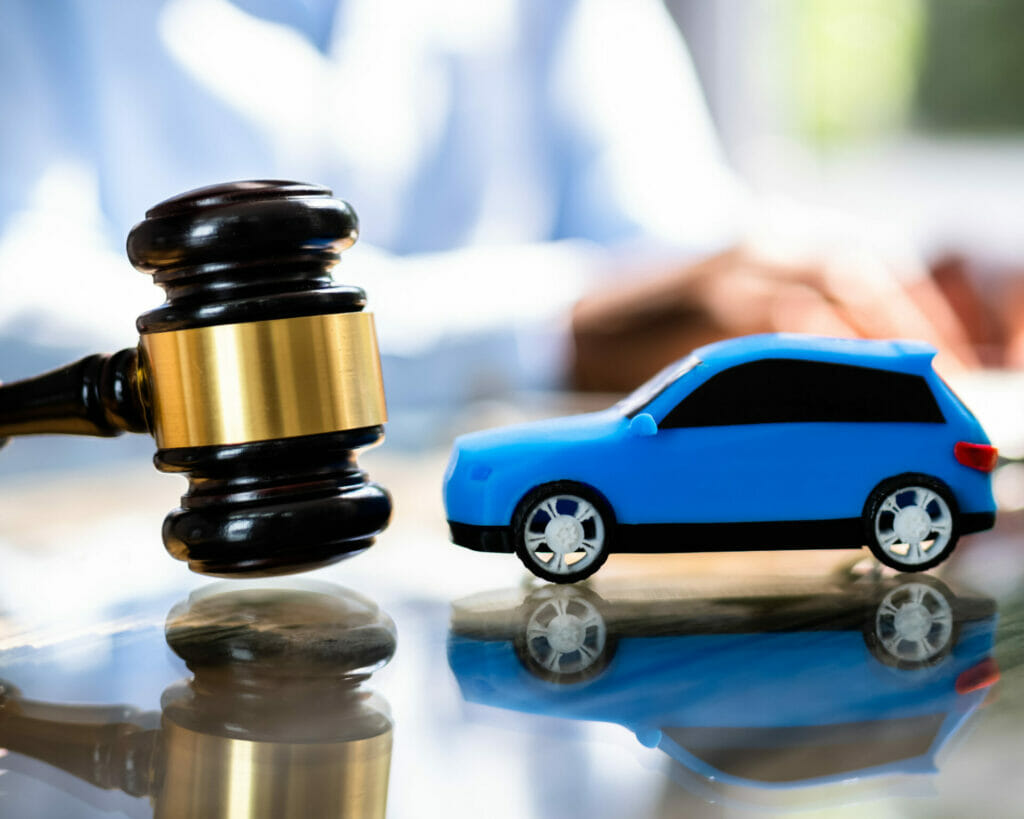 A gavel sits on a table next to a blue car involved in an auto accident.