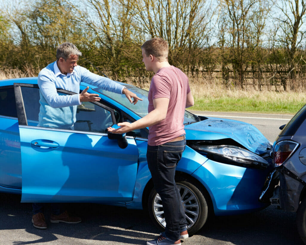 Two men standing next to a blue car after a car accident.