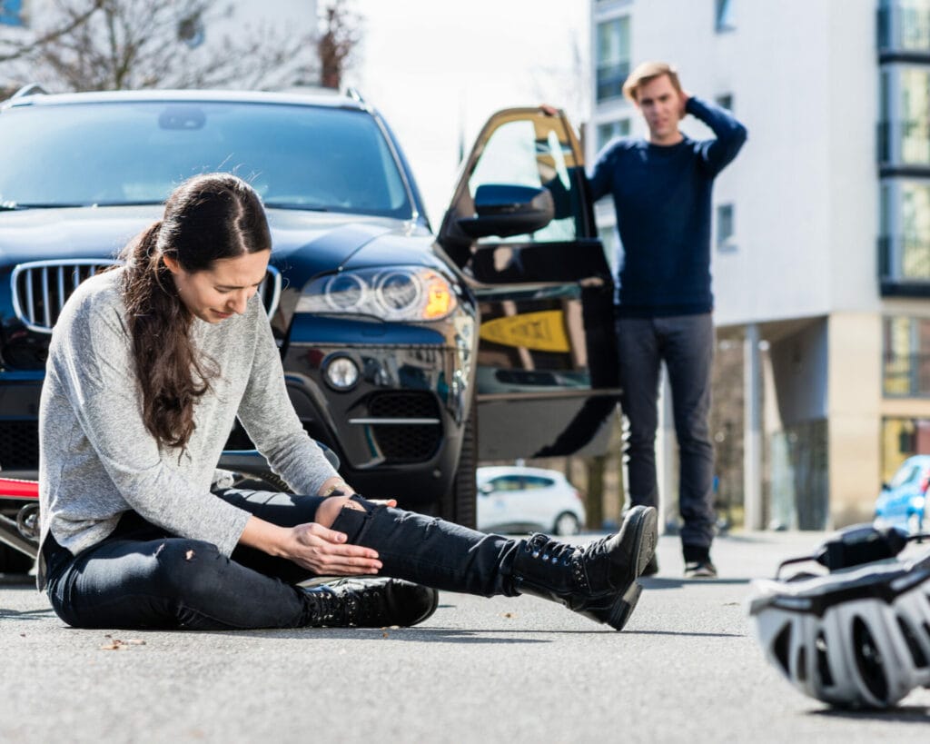The Mike Hostilo Law Firm - A woman sitting on the ground next to a car having a scarring injuries.