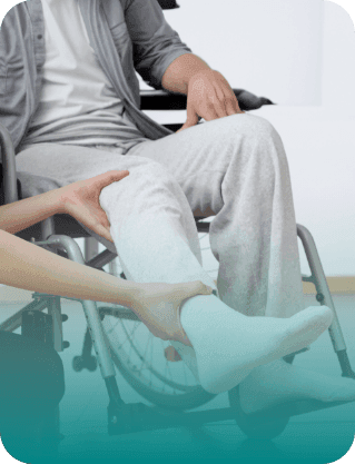 A close-up of a healthcare professional’s hands supporting and lifting the leg of a patient sitting in a wheelchair during a rehabilitation session.