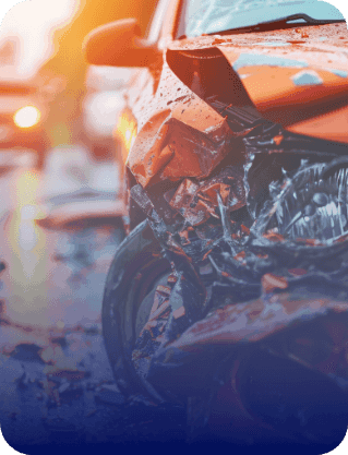 Orange car with major front-end damage from a collision; blurred car lights in the background.