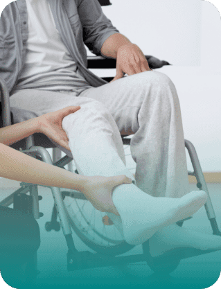 Caregiver assists a person in a wheelchair, supporting and examining the person’s injured leg.